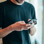 Mężczyzna w czarnej koszulce korzystający ze smartfona przy oknie z rośliną